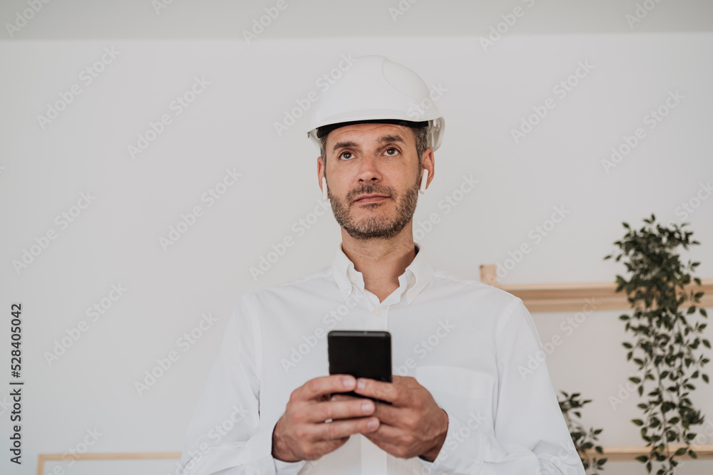 Engineer wearing hardhat holding mobile phone in office Engineer wearing hardhat holding mobile phone in office