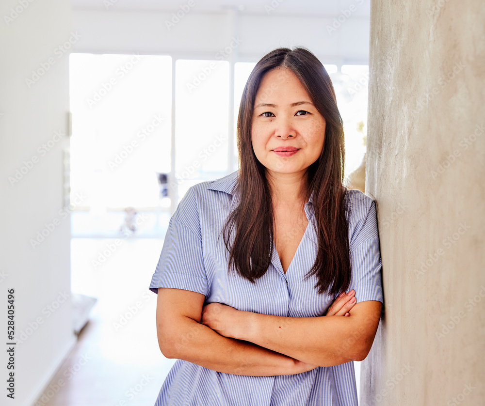 Smiling woman with arms crossed leaning on wall at home Smiling woman with arms crossed leaning on wall at home