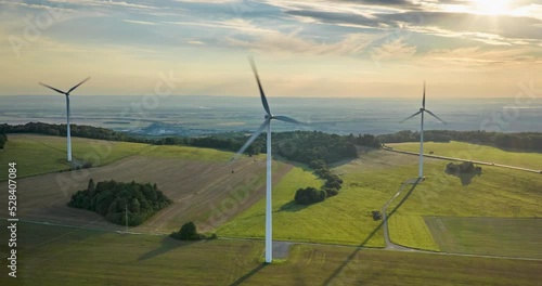 Hyperlapse, aerial view of wind turbine in full operation, spinning propellers, dramatic sky, windy day, sunset-lit landscape in the background, aerial timalapse footage. photo