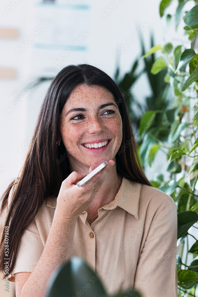 Happy businesswoman sending voicemail though smart phone in office
