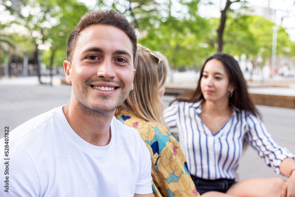Smiling young man sitting with friends talking at park Smiling young man sitting with friends talking at park
