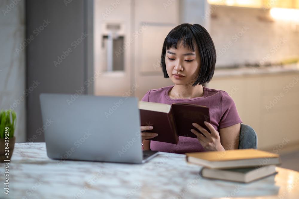 Pretty young asian girl reading a book and looking involved Pretty young asian girl reading a book and looking involved