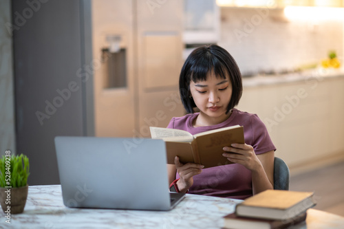 Pretty young asian girl reading a book and looking involved