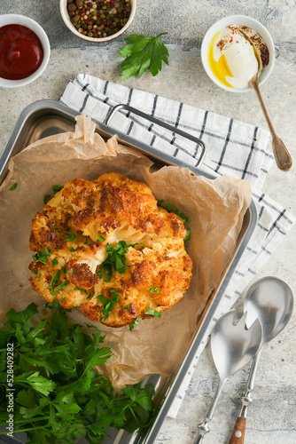 Baked cauliflower. Oven or whole baked cauliflower spices and herbs server on wooden rustic board on old grey background table. Delicious cauliflower. Eyal Shani dish. Perfect tasty snack. photo