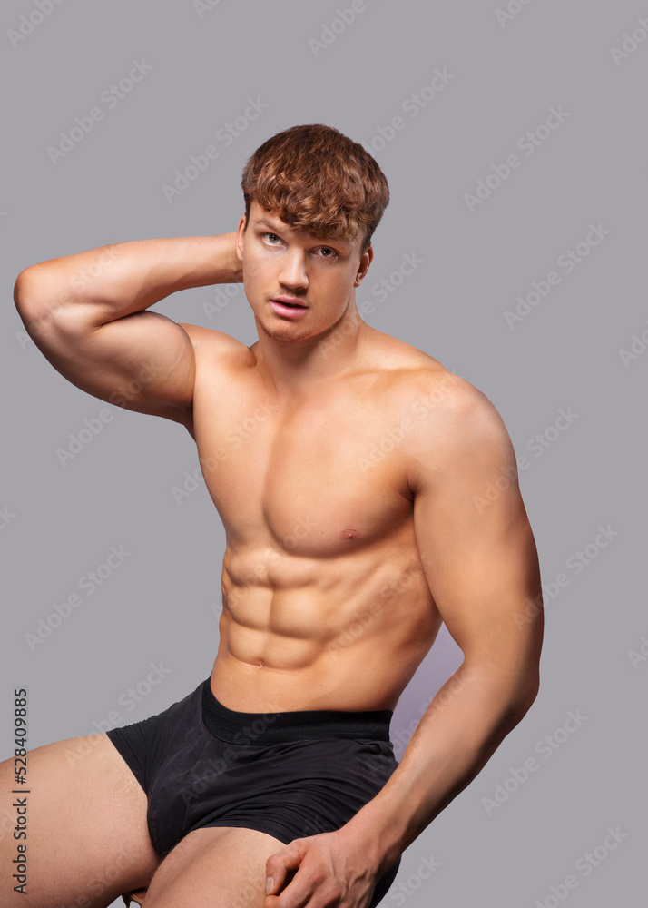 Fototapeta premium Advertising banner with young handsome caucasian athletic man on gray background. Portrait of man with beautiful athletic body who is dressed boxers and posing near copy space.