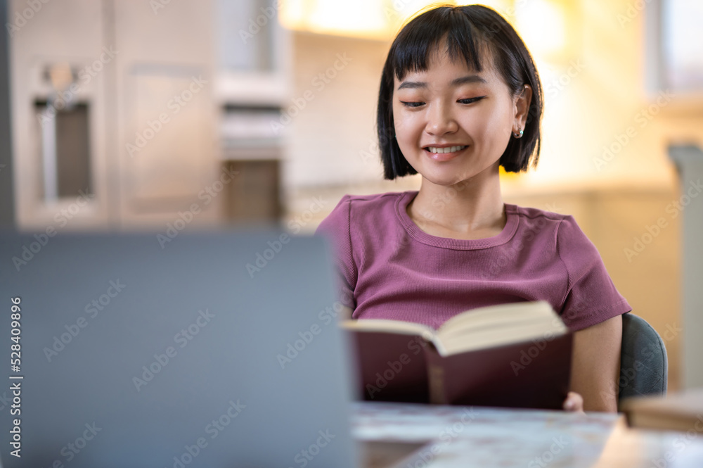 A girl in violet tshirt sitting at the laptop and looking happy A girl in violet tshirt sitting at the laptop and looking happy