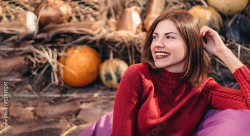 Portrait of a woman smiling against the background of straw and autumn decor with pumpkins