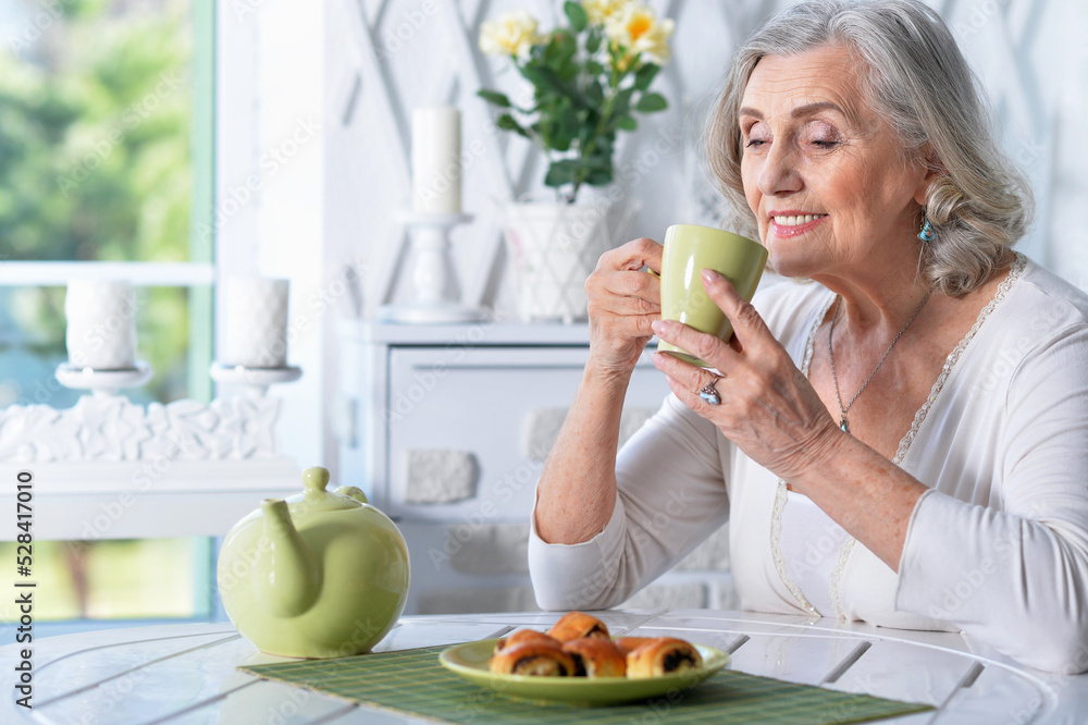Beautiful smiling senior woman drinking tea while sitting at kitchen table