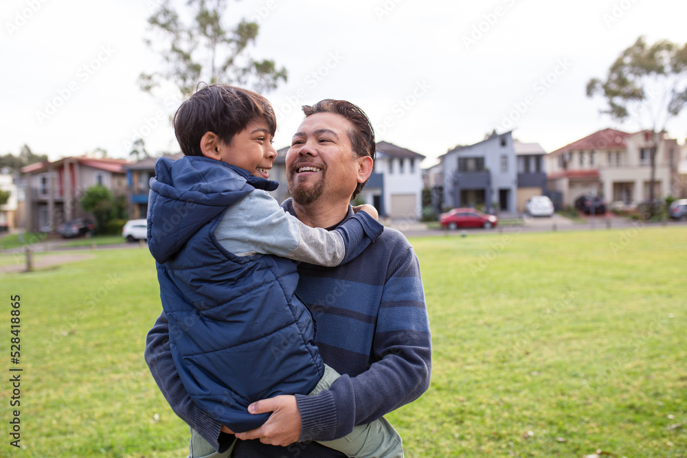 middle aged man wearing blue sweatshirt carrying a smiling boy in his arms on a big lawn middle aged man wearing blue sweatshirt carrying a smiling boy in his arms on a big lawn