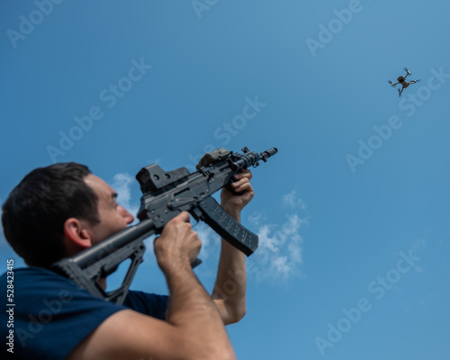 Caucasian man shoots a flying drone with a rifle.