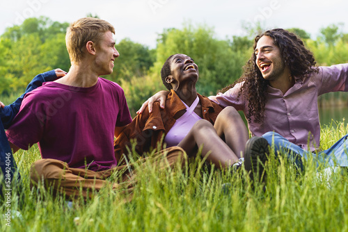 Cheerful multiethnic friends bonding and having fun hugging and laughing on the grass having fun together - Group of cheerful multiracial gen z young people gather on the grass 