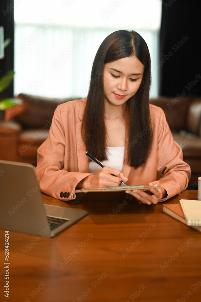 Charming asian woman sitting front of laptop and using digital tablet at her home office Charming asian woman sitting front of laptop and using digital tablet at her home office