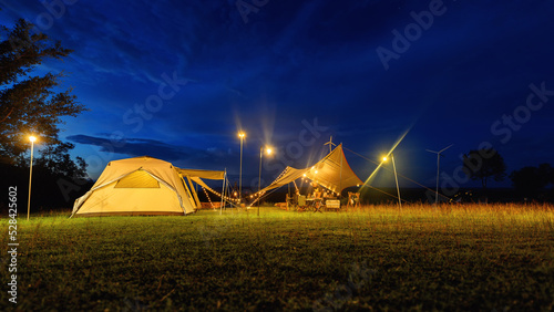 Φωτογραφία Outdoor camping tent with tarp or flysheet on grass courtyard and warm night light under dark blue sky twilight time, family vacation picnic on holiday relax, Overview of camping of family tourist