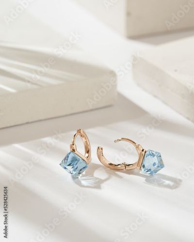 Golden earrings with square shaped light blue crystals and diamonds isolated on white background. Fashionable jewelry.