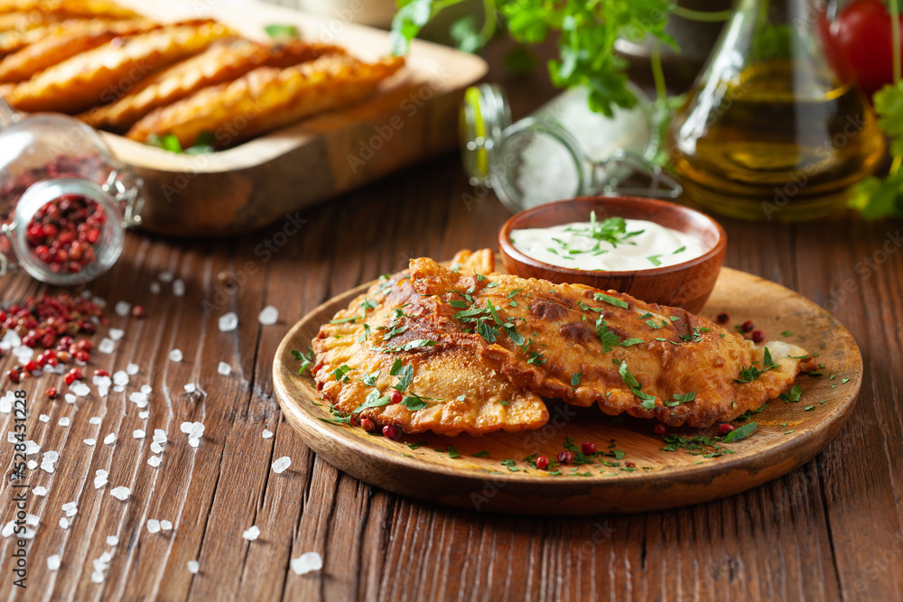 Traditional cheebureki, served on a wooden plate with sauce. Traditional cheebureki, served on a wooden plate with sauce.