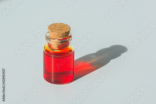 A bottle of red liquid. Aromatic oil of scarlet color in a glass tube.