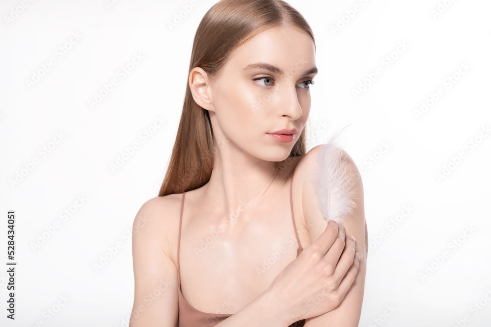 Beautiful female fashion model with glowing facial skin holding feather, looking aside on white background. Young woman advertising skincare treatment cosmetics, make up products for natural beauty. Beautiful female fashion model with glowing facial skin holding feather, looking aside on white background. Young woman advertising skincare treatment cosmetics, make up products for natural beauty.