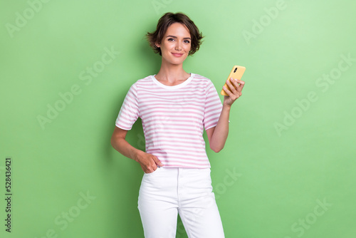 Photo of young pretty attractive positive good cute woman hold her new smartphone showing app for dating isolated on green color background