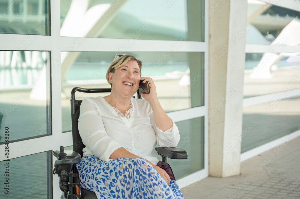 an elegant woman laughs while sitting in a wheelchair talking on the cell phone an elegant woman laughs while sitting in a wheelchair talking on the cell phone