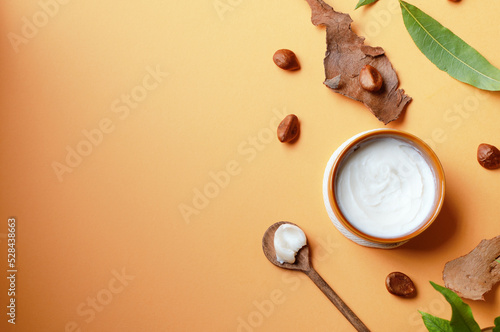 Unrefined shea butter with nuts and leaves on beige background, top view, copy space.