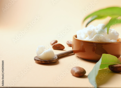 Unrefined shea butter with nuts and leaves on beige light background.