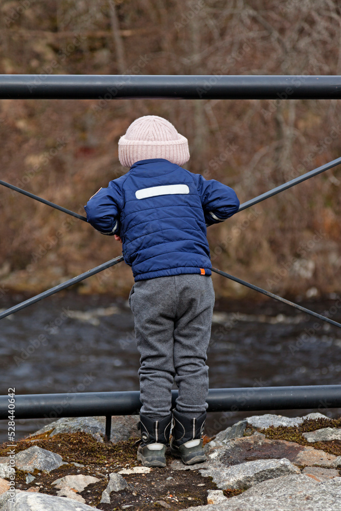 Savar, Norrland Sweden - May 11, 2021: little guy stands with his back to the river and looks out Savar, Norrland Sweden - May 11, 2021: little guy stands with his back to the river and looks out