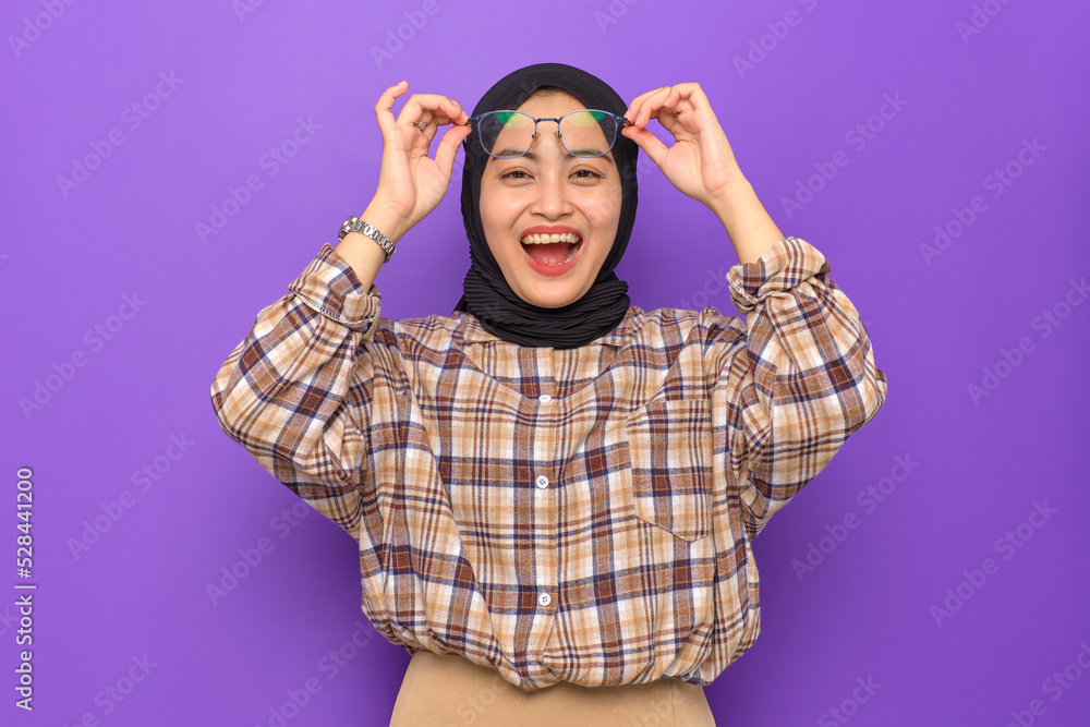 Amazed young Asian woman in plaid shirt taking off glasses with open mouth isolated on purple background Amazed young Asian woman in plaid shirt taking off glasses with open mouth isolated on purple background