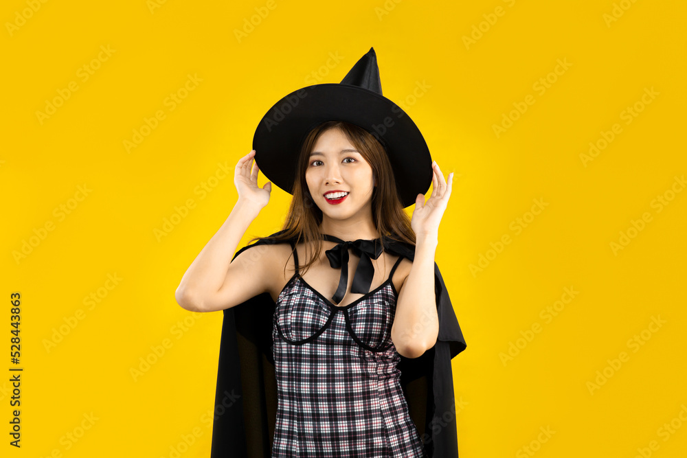 Young asian woman wearing witch hat and witchcraft and black dress posing on yellow color background for halloween concept theme. Young asian woman wearing witch hat and witchcraft and black dress posing on yellow color background for halloween concept theme.
