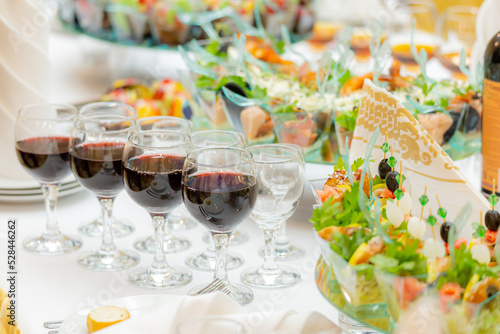 Glasses of red wine, delicacies, snacks and desserts on luxuriously served buffet tables. Restaurant business, catering.