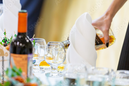 The waiter pours whiskey or cognac into a glass. Buffet tables at the event.