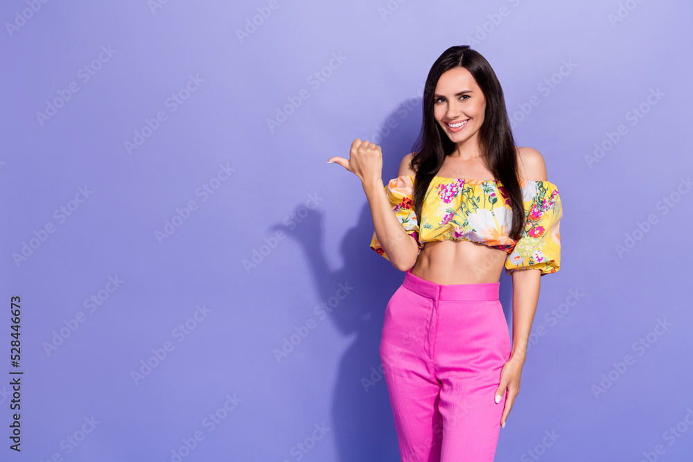 Photo of nice cheerful lady indicate thumb finger empty space isolated on violet color background Photo of nice cheerful lady indicate thumb finger empty space isolated on violet color background