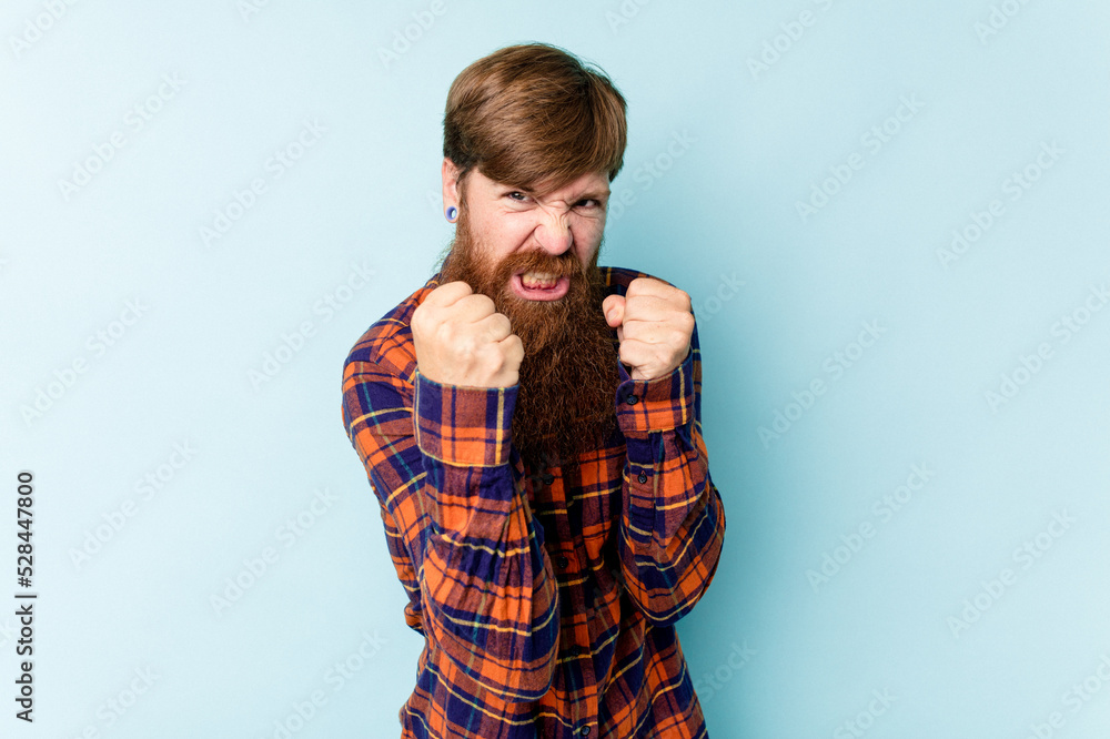 Young caucasian red-haired man isolated on blue background upset screaming with tense hands. Young caucasian red-haired man isolated on blue background upset screaming with tense hands.