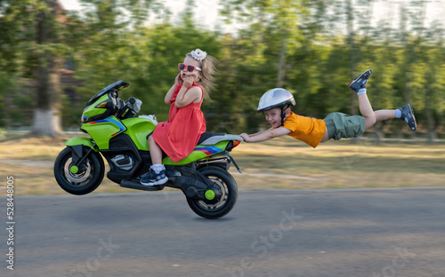 Children ride in the park on a children's electric car. A comic plot in which a boy holds onto the seat of a motorcycle and flies in the air surprises the girl.