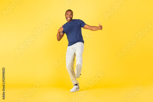 Happy African American Male Gesturing Thumbs Up Over Yellow Background