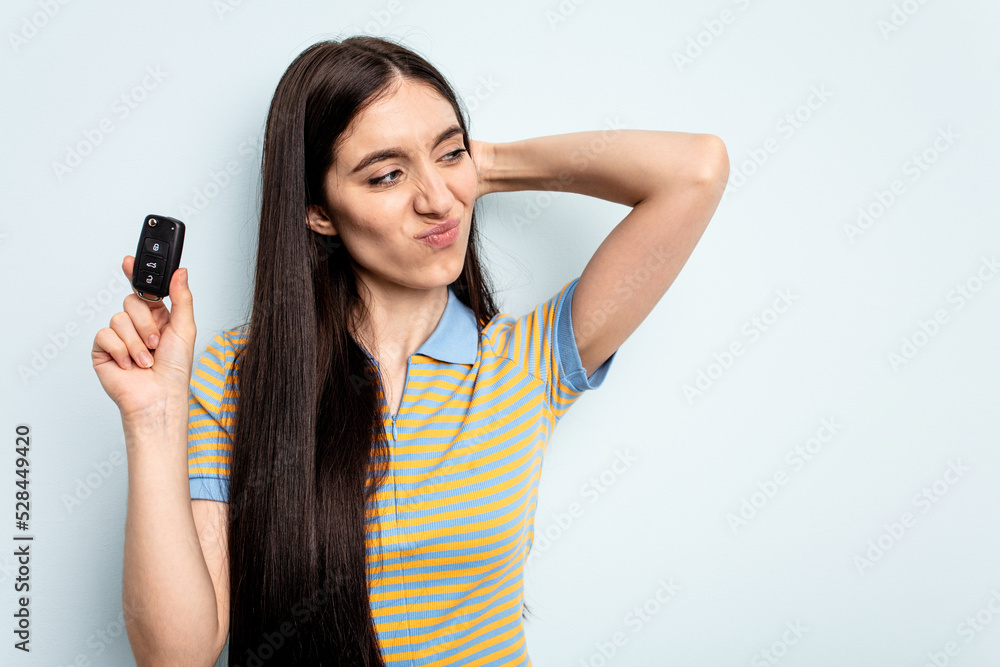 Young caucasian woman holding car keys isolated on blue background touching back of head, thinking and making a choice. Young caucasian woman holding car keys isolated on blue background touching back of head, thinking and making a choice.