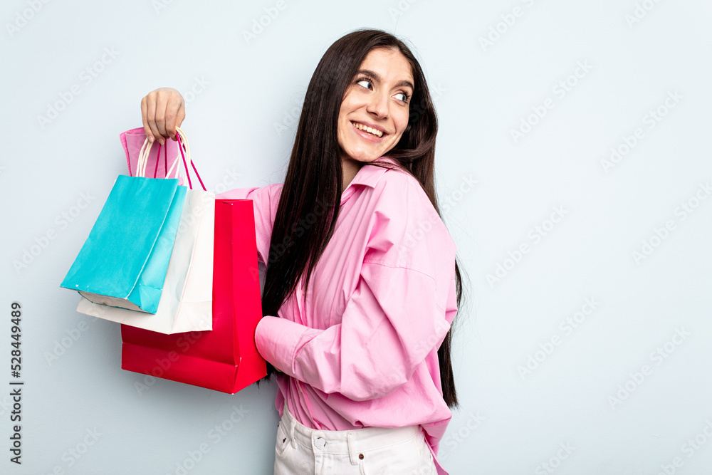 Young caucasian woman going to buy some clothes isolated on blue background looks aside smiling, cheerful and pleasant. Young caucasian woman going to buy some clothes isolated on blue background looks aside smiling, cheerful and pleasant.