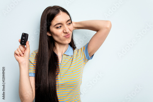 Young caucasian woman holding car keys isolated on blue background touching back of head, thinking and making a choice.