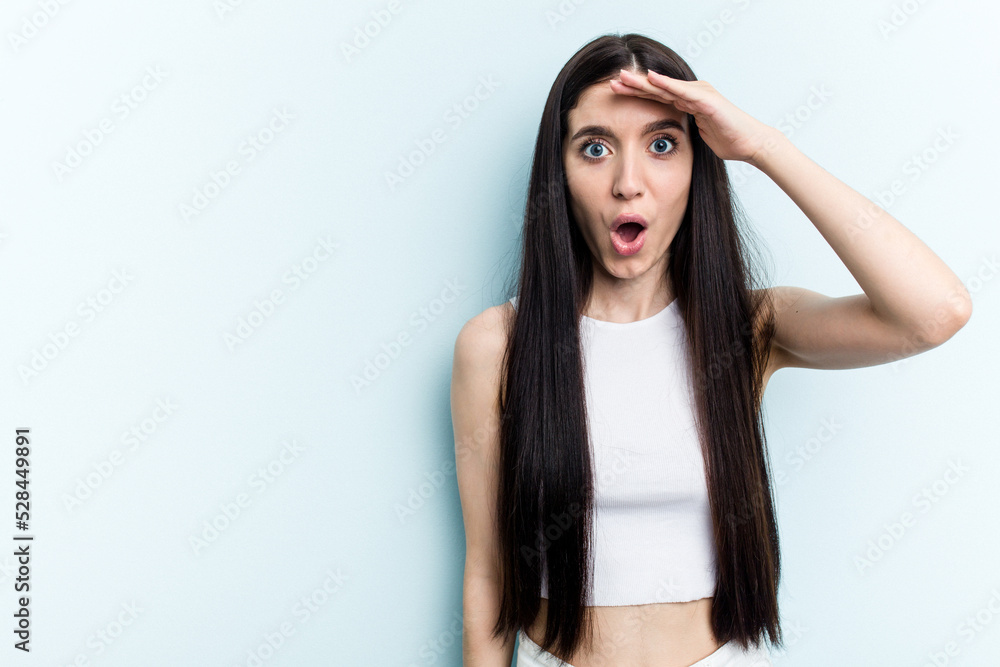 Young caucasian woman isolated on blue background shouts loud, keeps eyes opened and hands tense.