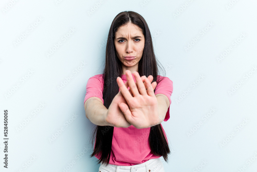 Young caucasian woman isolated on blue background standing with outstretched hand showing stop sign, preventing you. Young caucasian woman isolated on blue background standing with outstretched hand showing stop sign, preventing you.