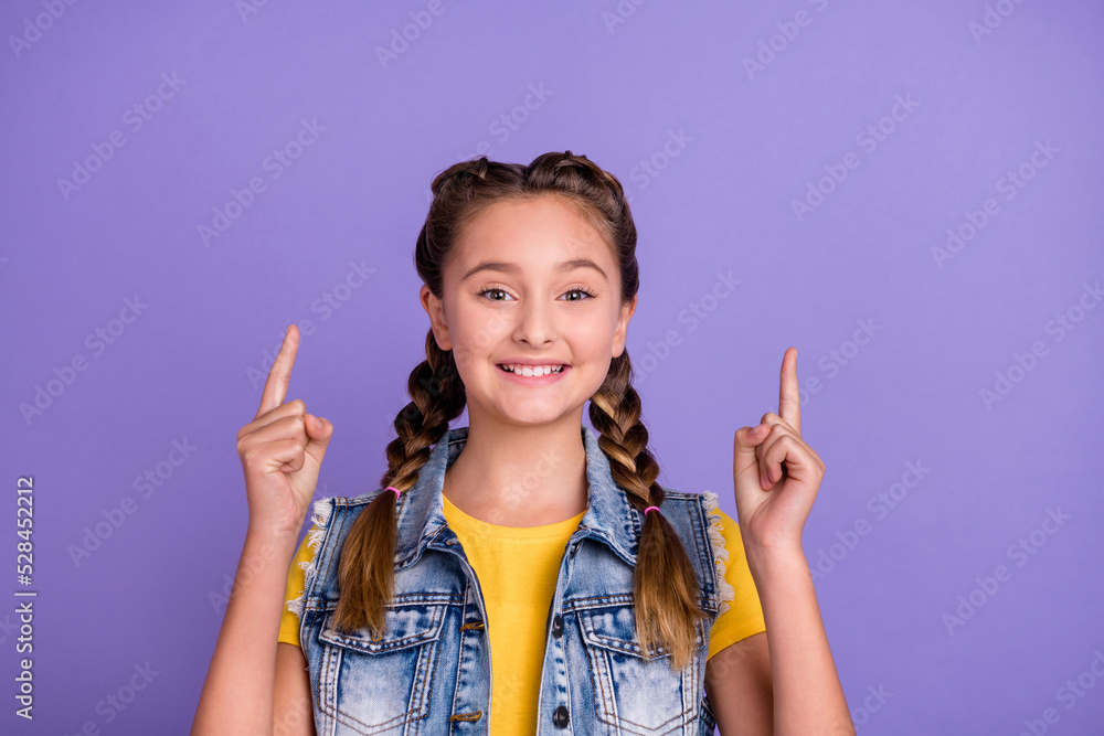 Photo of funky little blond girl index up wear yellow t-shirt jeans vest isolated on violet color background Photo of funky little blond girl index up wear yellow t-shirt jeans vest isolated on violet color background