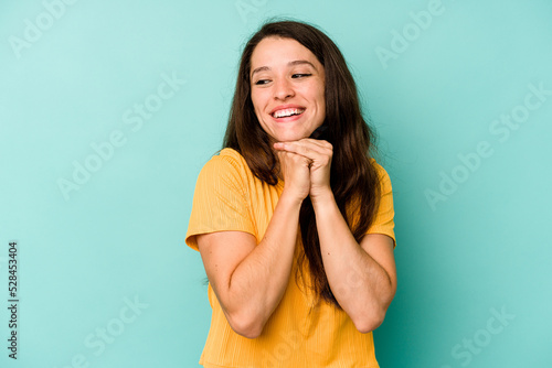 Young caucasian woman isolated on blue background keeps hands under chin, is looking happily aside.