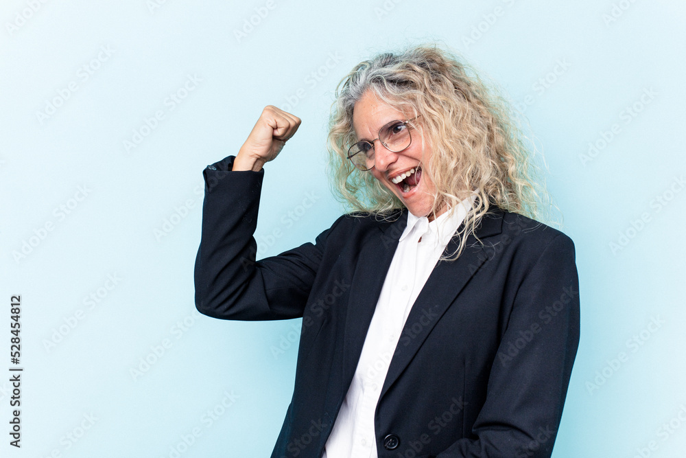 Middle age caucasian business woman isolated on blue background raising fist after a victory, winner concept. Middle age caucasian business woman isolated on blue background raising fist after a victory, winner concept.