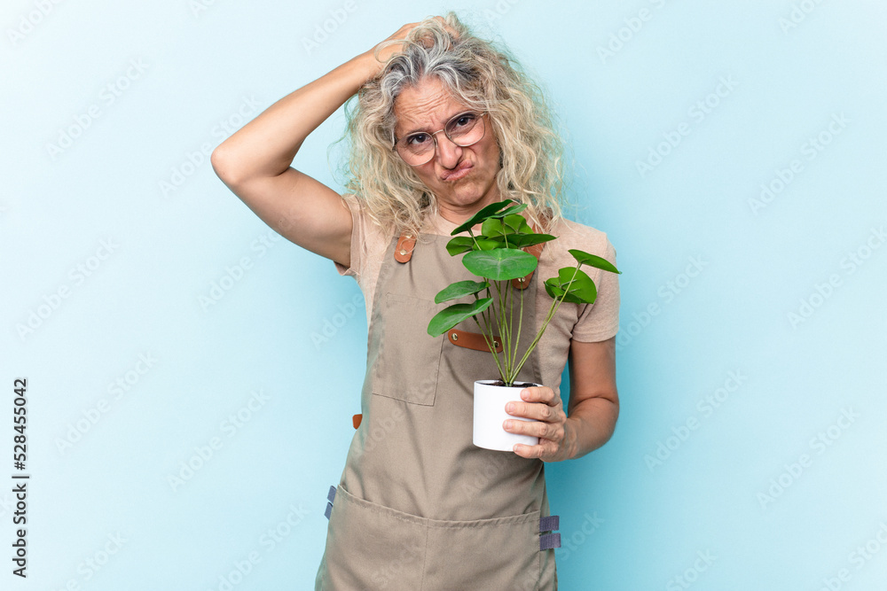 Middle age gardener woman holding a plant isolated on blue background being shocked, she has remembered important meeting. Middle age gardener woman holding a plant isolated on blue background being shocked, she has remembered important meeting.