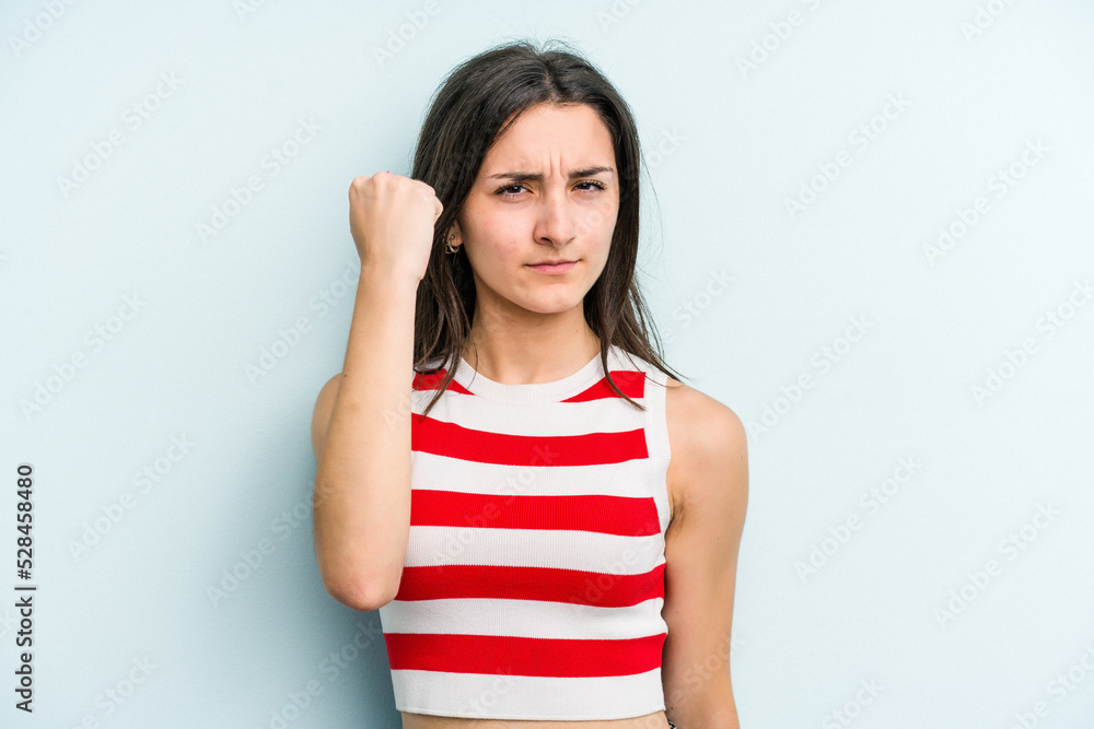 Young caucasian woman isolated on blue background showing fist to camera, aggressive facial expression. Young caucasian woman isolated on blue background showing fist to camera, aggressive facial expression.