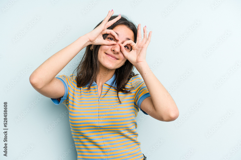 Young caucasian woman isolated on blue background showing okay sign over eyes Young caucasian woman isolated on blue background showing okay sign over eyes