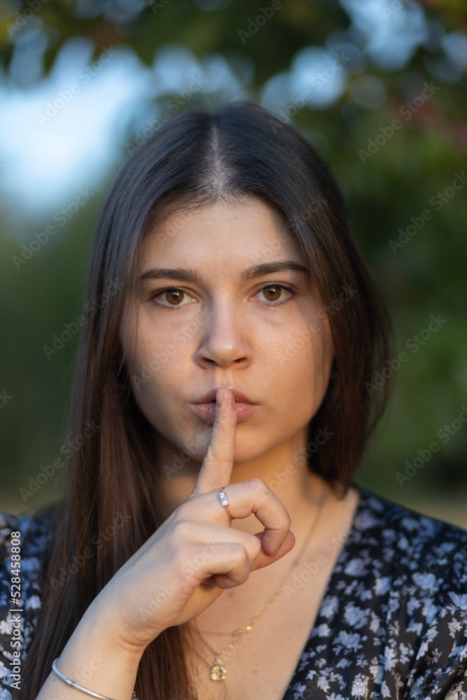 Portrait of beautiful young girl with long hair holding a finger to her lips with a face expressing fear or ordering silence, Poland Portrait of beautiful young girl with long hair holding a finger to her lips with a face expressing fear or ordering silence, Poland