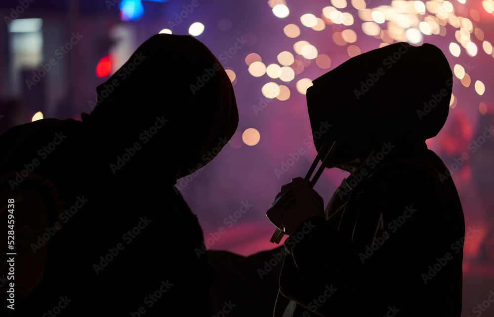 silhouette of two hooded men and fireworks in the background. selective focus blurred background silhouette of two hooded men and fireworks in the background. selective focus blurred background