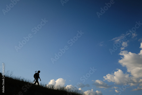 Photo Silhouette of a backpacker walking down the mountainside against a blue sky with clouds