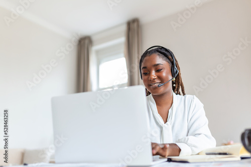 Happy young woman working on laptop while talking to customer on phone. Consulting corporate client in conversation with customer using computer. Service desk consultant talking in a call center.