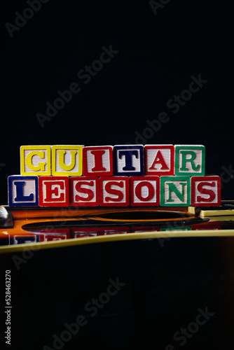 Word or phrase Guitar Lessons made with letter cubes, standing on guitar.